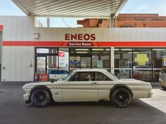 an old white car is parked in front of a gas station with the sign eneos service room