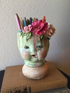 a vase with pencils sticking out of it's head on top of a stack of books