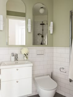 a white toilet sitting next to a sink in a bathroom under a mirror with lights on it