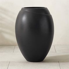 a large black vase sitting on top of a white tile floor next to a wall