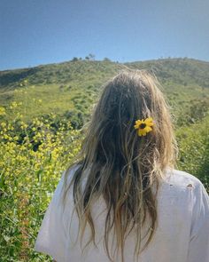 the back of a woman's head with a flower in her hair standing in a field