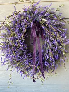 a purple wreath hanging on the side of a building with lavender flowers and green leaves