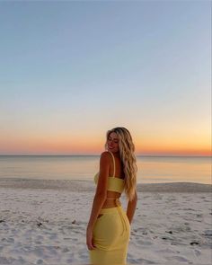 a woman standing on top of a sandy beach next to the ocean wearing a yellow dress