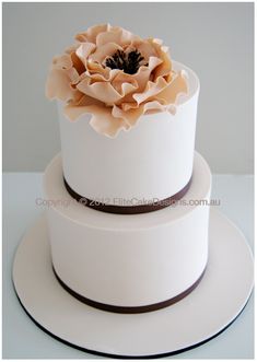 a three tiered white cake with a flower on the top and brown ribbon around it