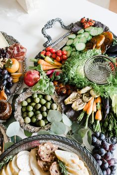 an assortment of fruits and vegetables are arranged in bowls on a white tablecloth with silver trays