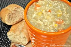 an orange cup filled with soup next to some bread