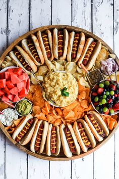 a platter filled with hot dogs, vegetables and dips