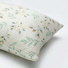 a white pillow with green and yellow floral print on the front, sitting on a white surface