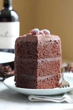 a slice of chocolate cake on a plate with a bottle of wine in the background