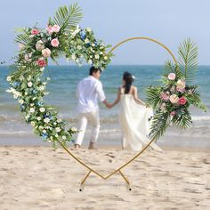 a man and woman holding hands in front of a heart shaped frame on the beach