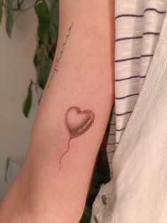 a woman's arm with a heart shaped balloon tattoo on the left side of her arm