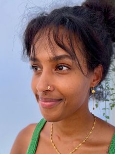 a close up of a person wearing a necklace and smiling at the camera with flowers in the background