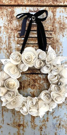 a book page paper flower wreath hanging on a black ribbon. Vintage Paper Wreath, Paper Flowers Out Of Book Pages, Paper Book Flowers, Books Sculpture, Recycled Book Crafts, Upcycled Books Crafts, Book Page Roses, Book Wreath, Book Page Flowers