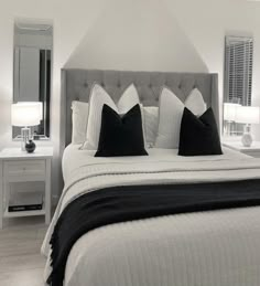 a white bed with black pillows and two lamps on either side of the headboard