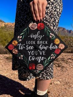 a woman is holding a black and white embroidered bag with flowers on it that says, only look back to see how far you've come