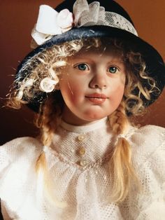 a doll with blonde hair wearing a black hat and white dress is looking at the camera