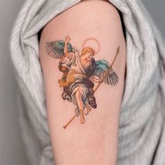 an angel tattoo on the arm of a woman's left arm, holding a stick and arrow