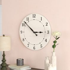 a white clock mounted to the side of a wall next to a lamp and vase