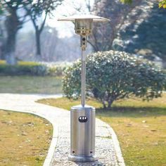 an outdoor patio heater in the middle of a walkway with trees and bushes behind it