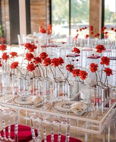 red flowers are in clear vases on display at a wedding reception with crystal chairs