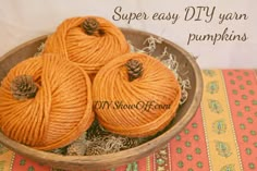 three balls of orange yarn in a bowl on a tablecloth with pine cones and twine