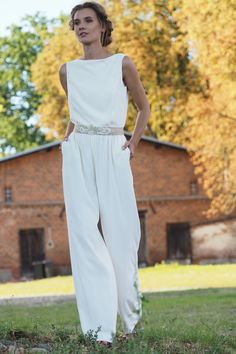 a woman is standing in the grass wearing a white jumpsuit with beaded belt