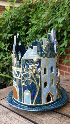 a ceramic castle sitting on top of a wooden table next to some trees and bushes