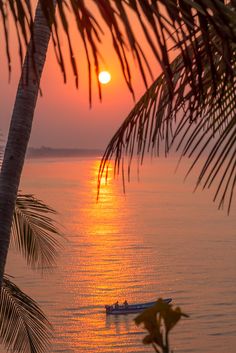 the sun is setting over the ocean with a boat in the water and palm trees