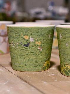 two cups with animals painted on them are sitting on a wooden table next to each other