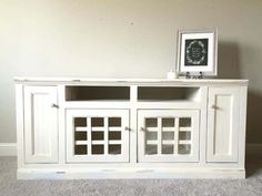 a white entertainment center with glass doors on the top and bottom, in front of a beige wall