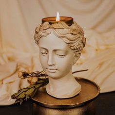 a white statue with a candle on top of it next to some dried flowers and leaves