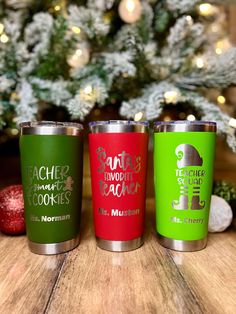 three different colored tumblers sitting on top of a wooden table next to a christmas tree