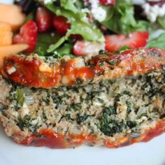 meatloaf with spinach, cheese and fruit on a white plate next to salad