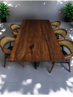 a wooden table surrounded by chairs and potted plants on the floor in front of it