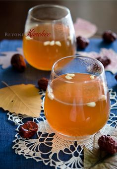 two glasses filled with liquid sitting on top of a blue table cloth next to leaves and nuts