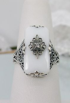 White Glass & Inset Gemstone (CZ, Moissanite, or Diamond) Intricate Filigree Ring Grace Design#233 Custom Made I now offer this lovely Antique Art Deco/Edwardian design ring in sterling silver. This gorgeous ring is set with a stunning floral filigree embellished white glass/resin with a centered inset 1mm white round cut CZ, Lab Moissanite, or Natural Diamond (Choose option above). The glass is 18mm Long by 19mm Wide. The ring sits 9mm North South on the finger and 10mm East West on the finger. Classic Sterling Silver Jewelry With Stone Setting, White Rings With Accent Stones For Formal Occasions, Formal White Rings With Accent Stones, Classic White Filigree Ring With Intricate Design, Ornate Diamond White Filigree Jewelry, Ornate Filigree Diamond White Jewelry, Ornate Diamond White Jewelry With Filigree, Victorian Diamond Jewelry With Intricate Design, Classic White Rings With Accent Stones