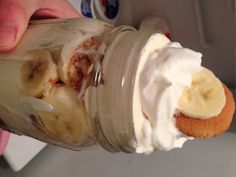 a person holding a mason jar filled with whipped cream and banana slices