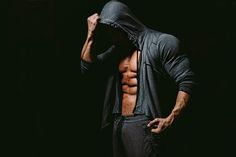 a shirtless man with no shirt standing in the dark holding his hood up to his face