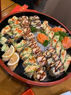 a platter full of sushi and other food items on a wooden table top