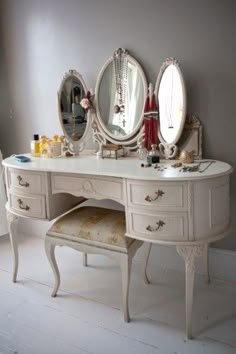 a white vanity with three mirrors on it and a stool in front of the mirror