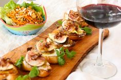 a wooden board topped with food next to a glass of wine