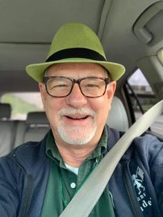 an older man wearing glasses and a green hat is sitting in the back seat of a car