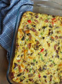 a casserole dish with vegetables and meat in it on a wooden table next to a blue towel