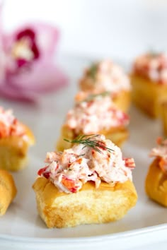 small appetizers are arranged on a white plate with pink flowers in the background