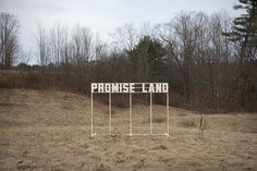 a sign that says promise land in front of some trees and bushes on the side of a hill