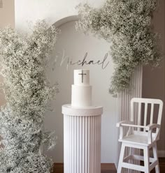 a cake sitting on top of a white pedestal next to a chair and table with flowers