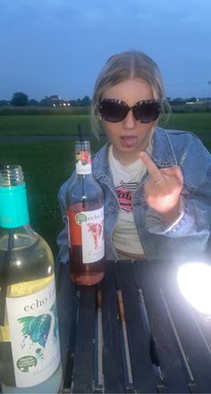 a woman sitting at a picnic table with two bottles of wine in front of her