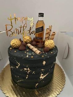 a birthday cake is decorated with gold and black icing, chocolate candies, and a bottle of booze