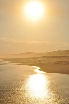 the sun shines brightly in the sky over an empty beach and body of water