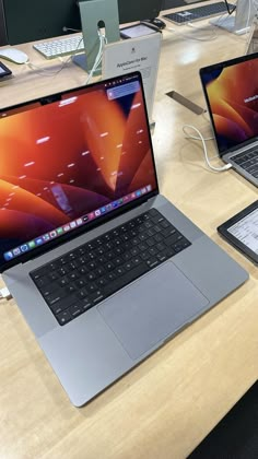 two laptops sitting on top of a wooden table next to each other in an office